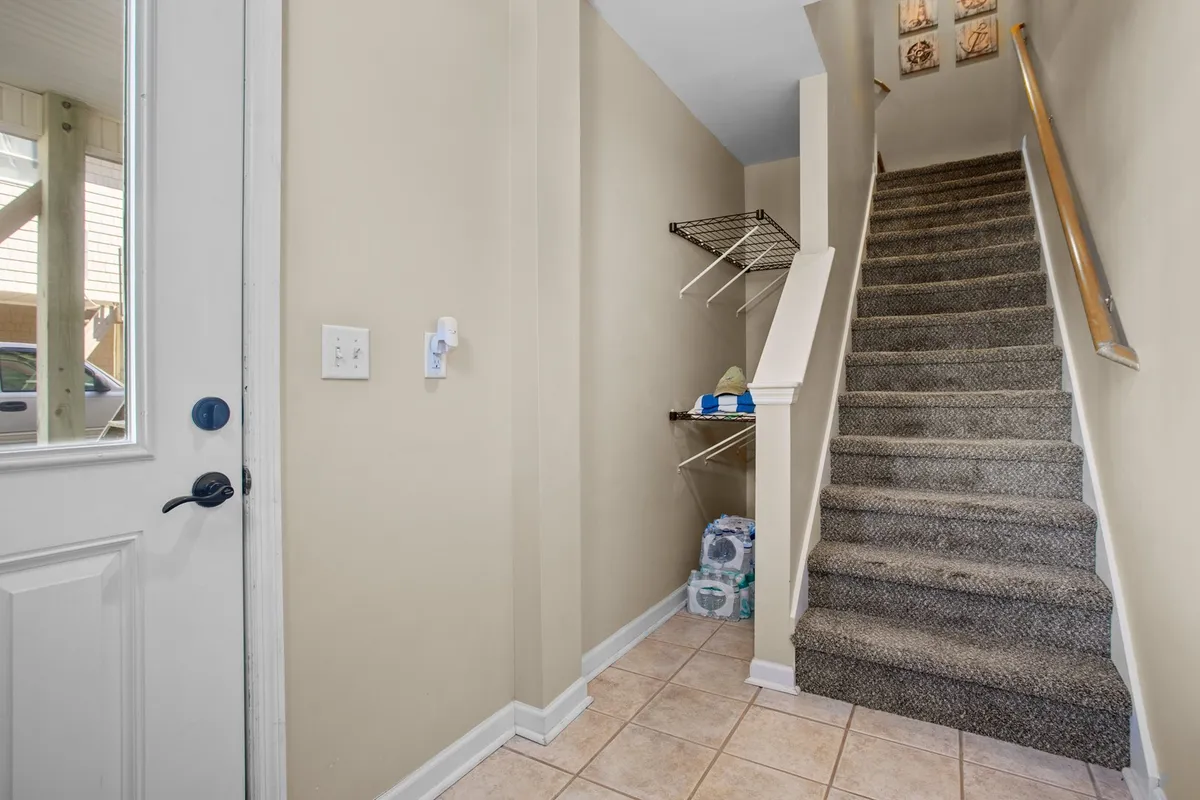 An inviting view of the home's entrance area, showing the entrance door, a staircase, and a shelf with assorted items. The space feels welcoming, organized, and hints at a smooth arrival experience.
