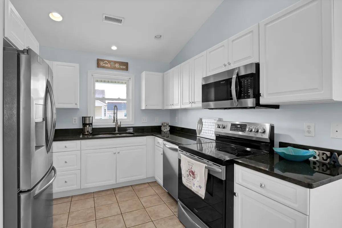 A bright and modern kitchen featuring stainless steel appliances, granite countertops, white cabinetry, and a window that brings in plenty of sunlight. The space is open and inviting, ideal for preparing meals and gathering with others.