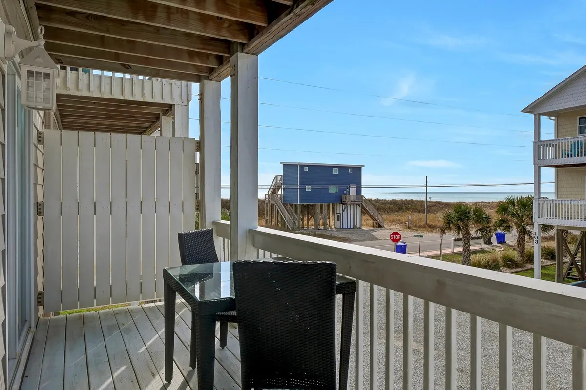 This image features a serene balcony with a table and chairs overlooking the beach and framed by palm trees. The tranquil scene evokes a sense of peaceful relaxation, perfect for enjoying morning coffee, reading, or watching a romantic sunrise or sunset with a loved one.