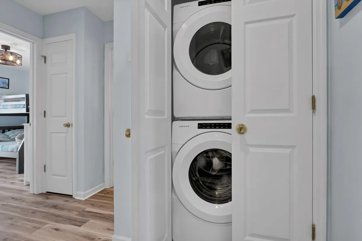 This image features a stacked washer and dryer in a compact laundry area with light blue walls. Doorways to other rooms are visible, conveying an organized, bright, and functional space for handling sandy swimsuits and towels after beach visits.